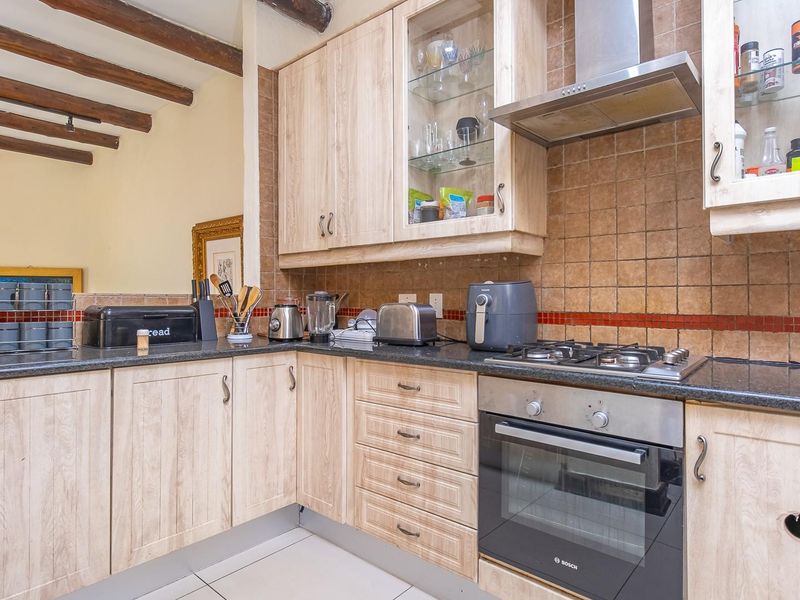 A functional kitchen featuring light wood cabinetry, granite countertops, built-in oven, gas hob, and rustic exposed timber ceiling beams.