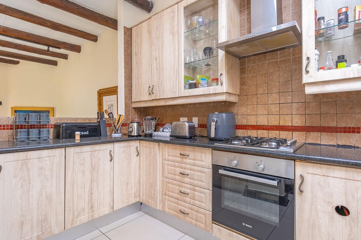 A functional kitchen featuring light wood cabinetry, granite countertops, built-in oven, gas hob, and rustic exposed timber ceiling beams.