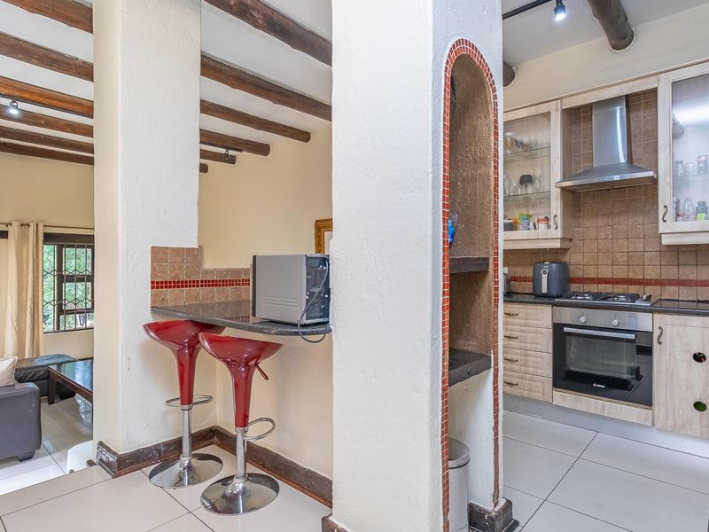 Open-plan kitchen and living area featuring exposed timber ceiling beams, tiled flooring, and a functional kitchen with built-in oven and hob.