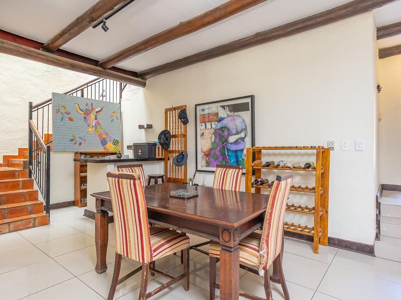 Dining area featuring exposed timber ceiling beams, ceramic floor tiles, and a distinctive terracotta tiled staircase with wrought iron railing.