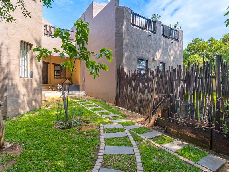 Rear exterior view of the townhouse featuring a stone paver pathway, landscaped garden area, and upper-level balcony with metal railings.