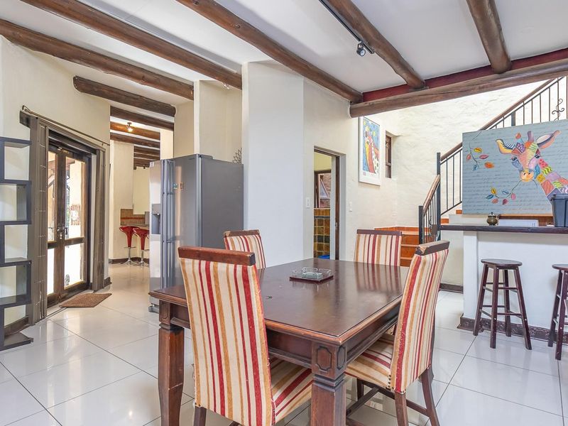 Open-plan living and dining area featuring exposed timber ceiling beams, tiled flooring, and a staircase with wrought iron railing.