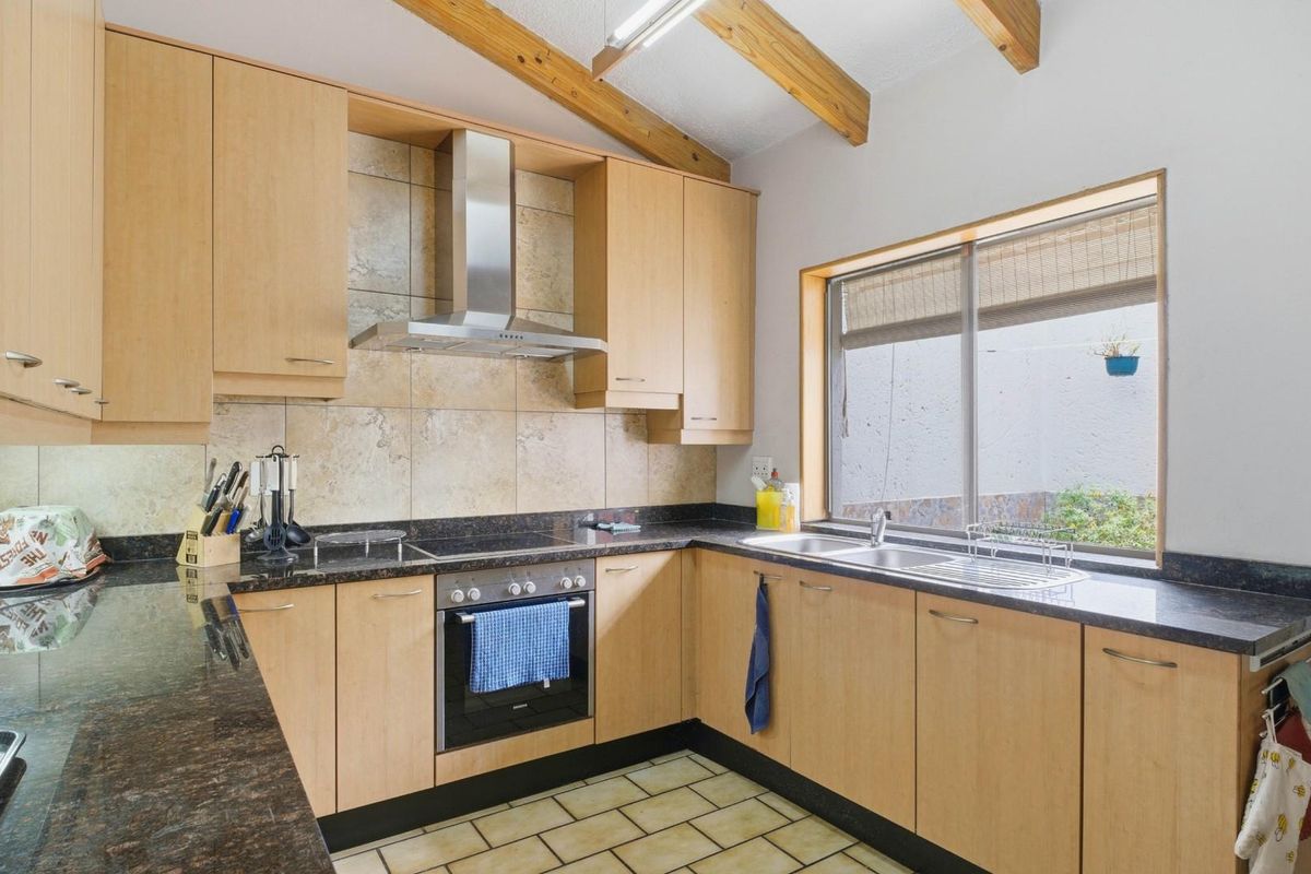 A functional kitchen featuring light wood cabinetry, dark granite countertops, a built-in oven with extractor fan, and exposed timber ceiling beams.