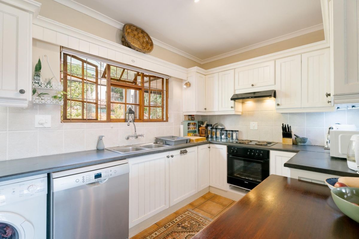 A well-maintained kitchen featuring white cabinetry, dark countertops, a built-in oven, extractor fan, and a double sink with a wooden-framed window.