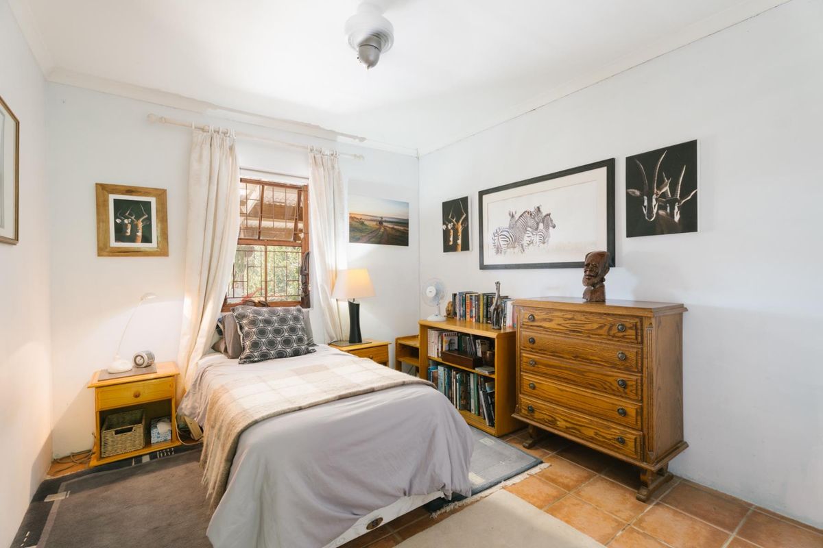 A cozy bedroom featuring terracotta floor tiles, a single window with natural light, and neutral wall finishes.