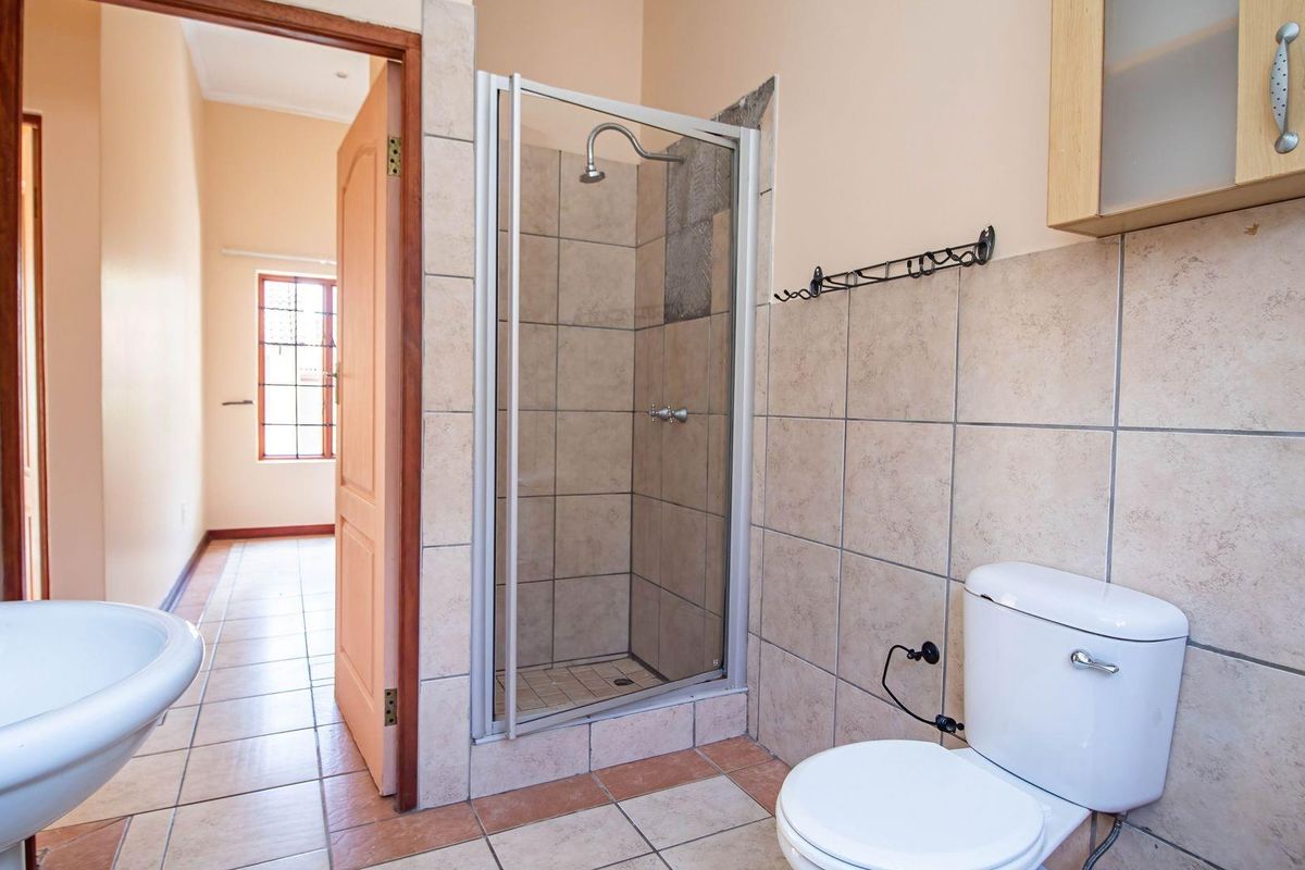 A functional bathroom featuring a tiled shower enclosure, pedestal basin, and standard toilet, with neutral wall tones and tiled flooring.