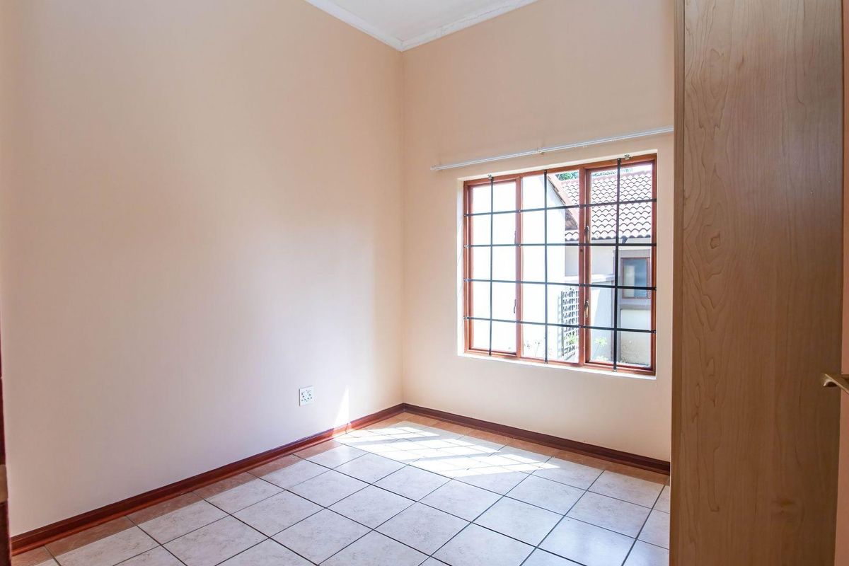 A bright, empty bedroom featuring tiled flooring, a window with security bars, and a wooden door, offering a clean canvas for personalization.
