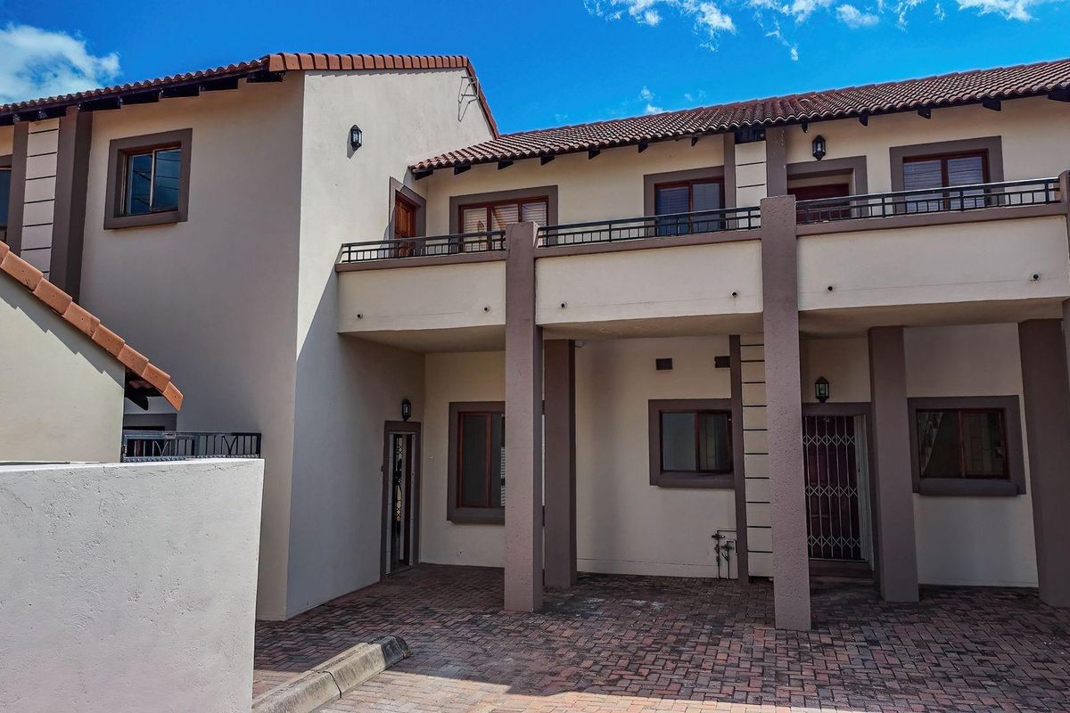 A view of the townhouse exterior featuring a paved courtyard, upper-level balcony with metal railings, and tiled roof structure.