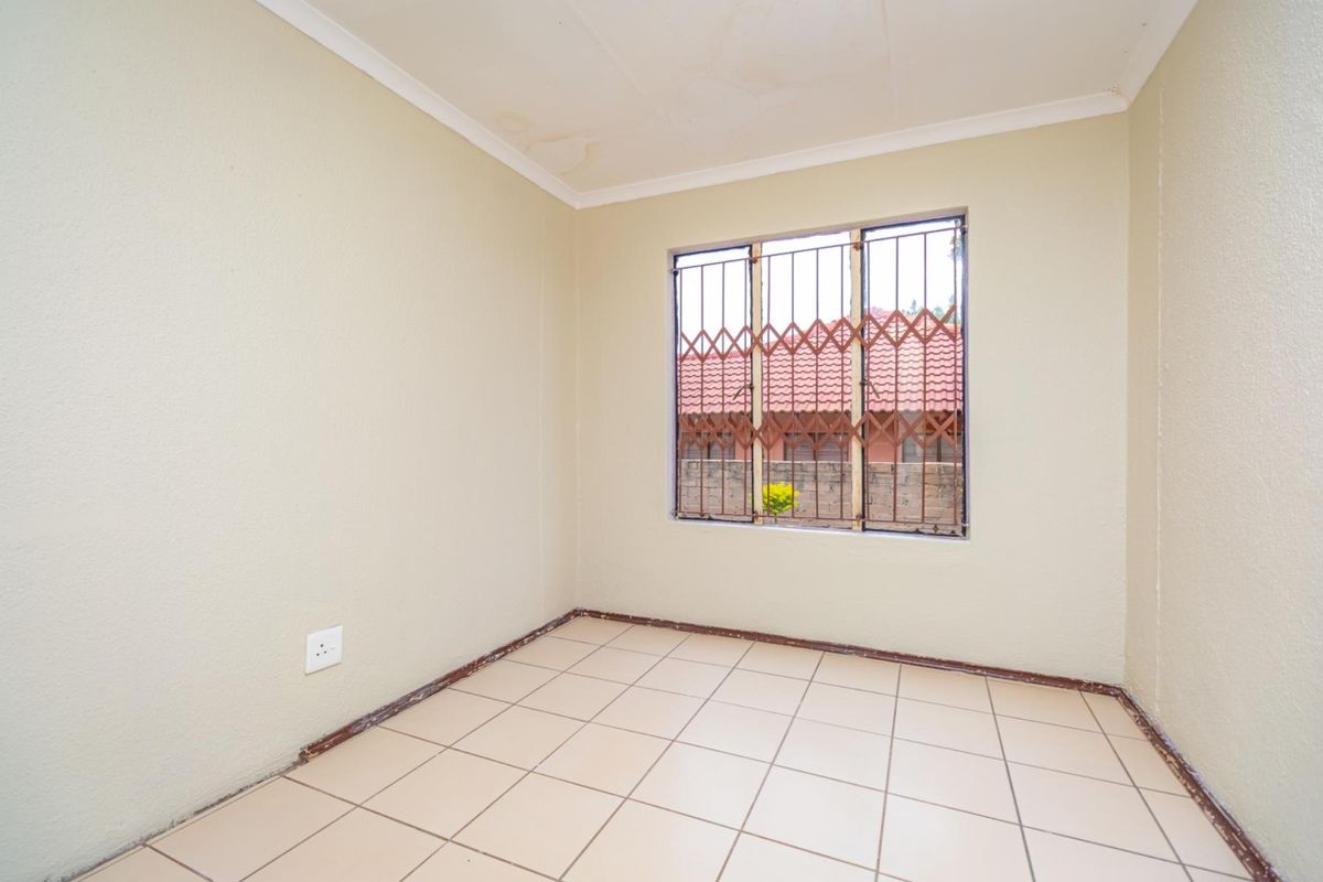 An empty bedroom featuring tiled flooring, a window with security bars, and neutral wall finishes, ready for personalization.