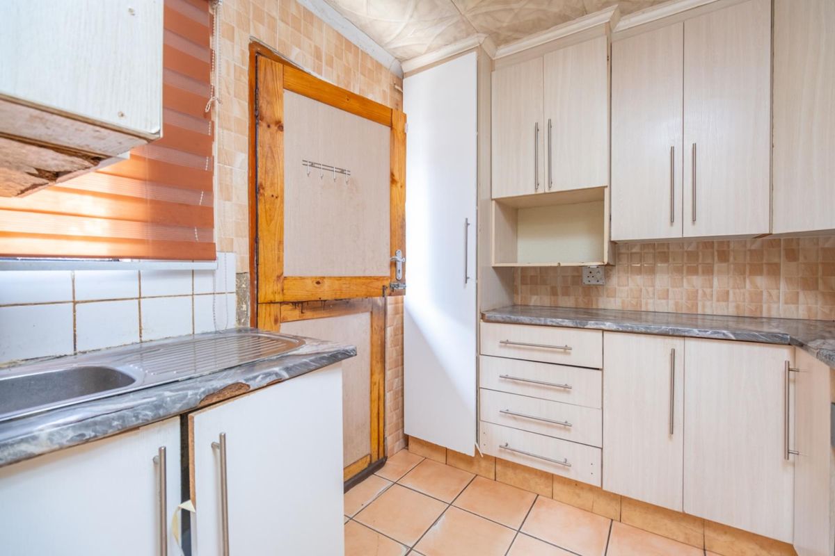 Compact kitchen featuring light-toned cabinetry, tiled flooring, and a stainless steel sink, offering a functional layout with potential for modernization.