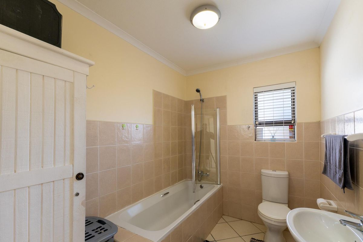 A functional bathroom featuring a bathtub with a glass shower screen, a standard toilet, and a pedestal sink with neutral wall tiling.
