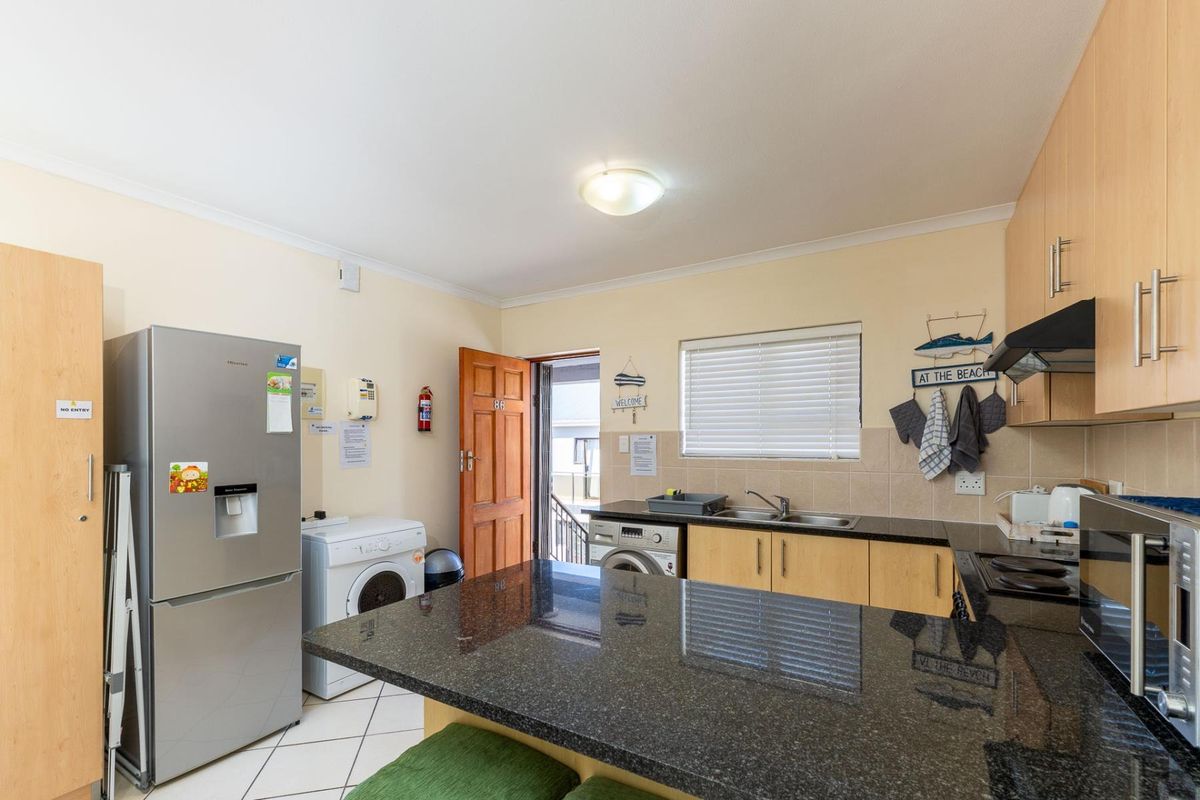 A functional kitchen featuring granite countertops, light wood cabinetry, a double sink, and integrated laundry appliances, with direct access to the exterior.
