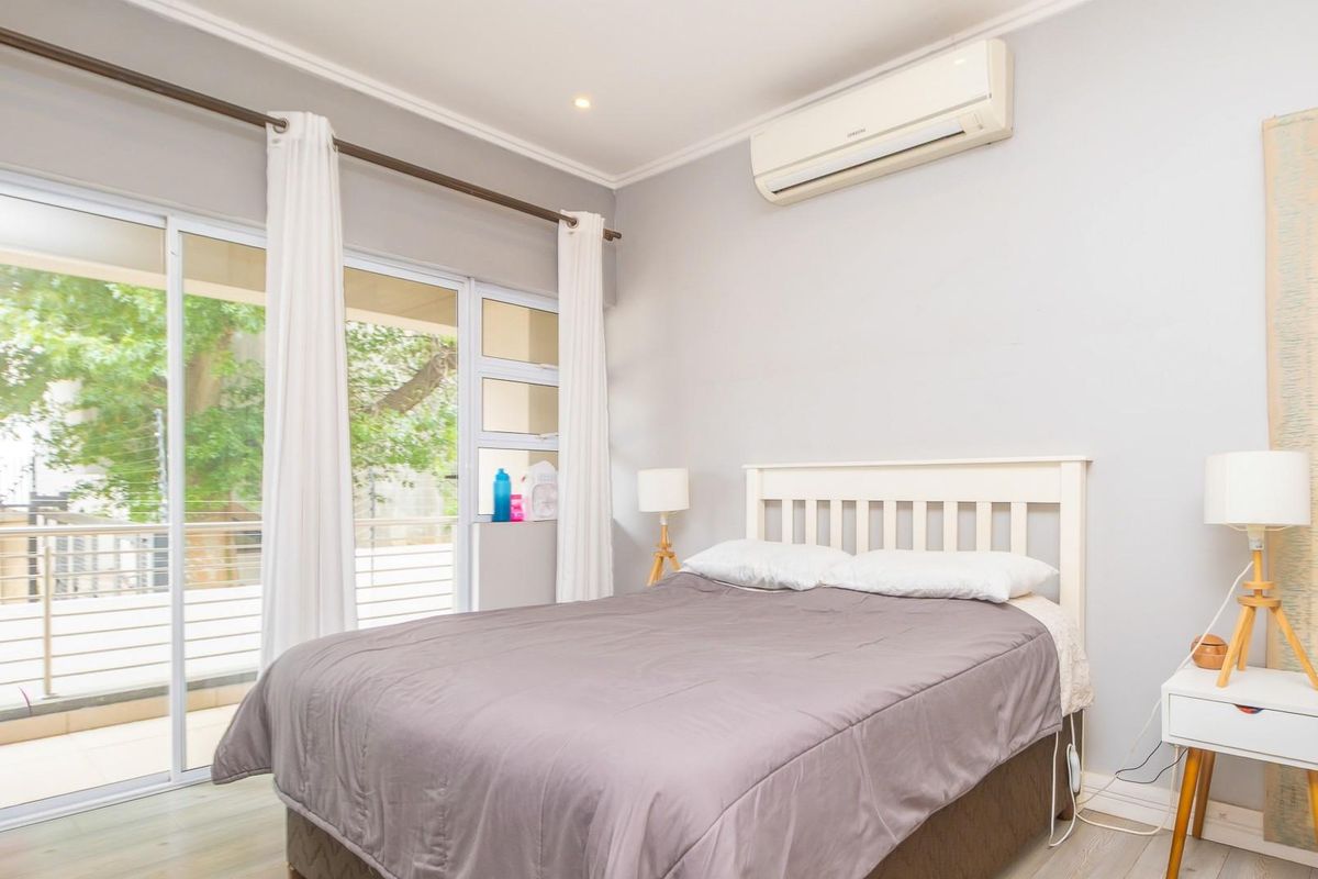 A well-maintained bedroom featuring laminate flooring, an integrated air conditioning unit, and large sliding glass doors providing direct access to a private balcony.