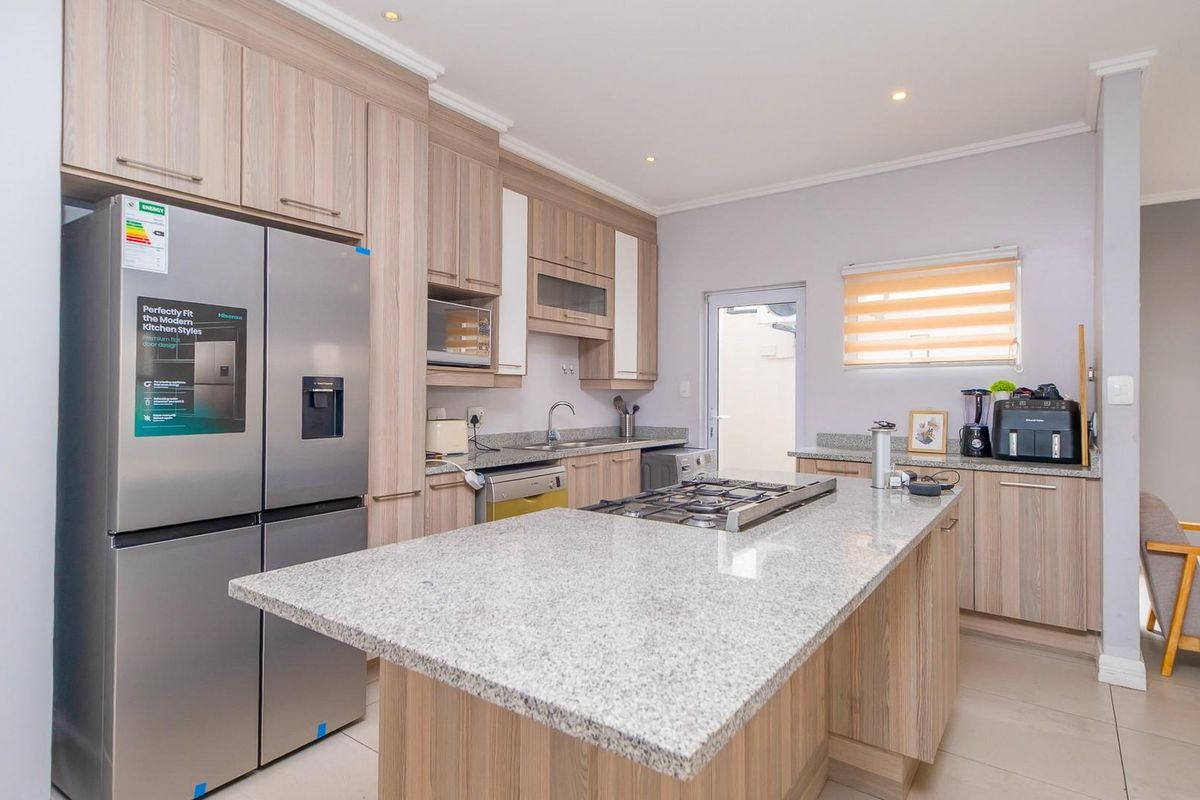 Modern kitchen featuring light wood cabinetry, granite countertops, a central island with a gas hob, and tiled flooring.