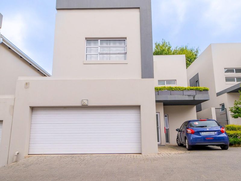 Modern townhouse exterior featuring a double garage, paved driveway, and a balcony with integrated planter box.