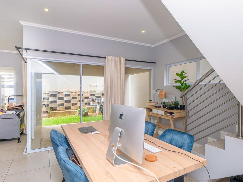 Bright open-plan living area featuring tiled floors, recessed lighting, and a modern staircase with metal balustrades, leading out to a private garden patio.