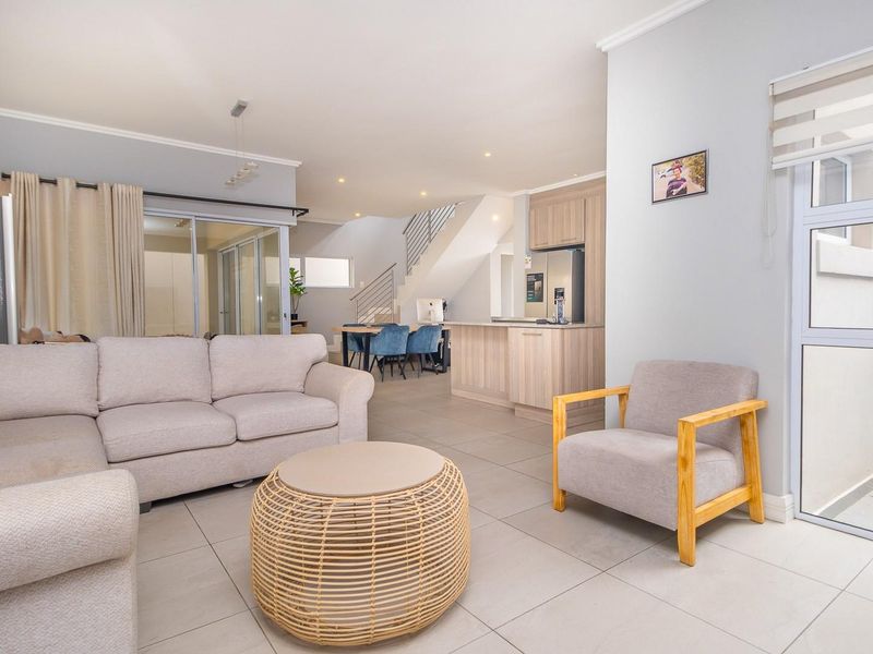 Spacious open-plan living area featuring tiled floors, recessed lighting, and a modern staircase, seamlessly connecting to the kitchen and outdoor access points.