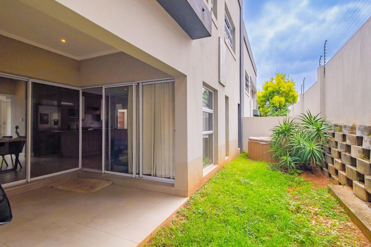 Rear view of the townhouse featuring a covered patio with tiled flooring, sliding glass doors, and a private garden area with a retaining wall.