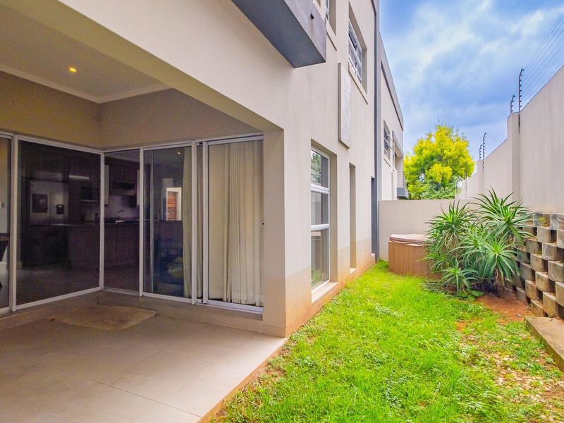 Rear view of the townhouse featuring a covered patio with tiled flooring, sliding glass doors, and a private garden area with a retaining wall.