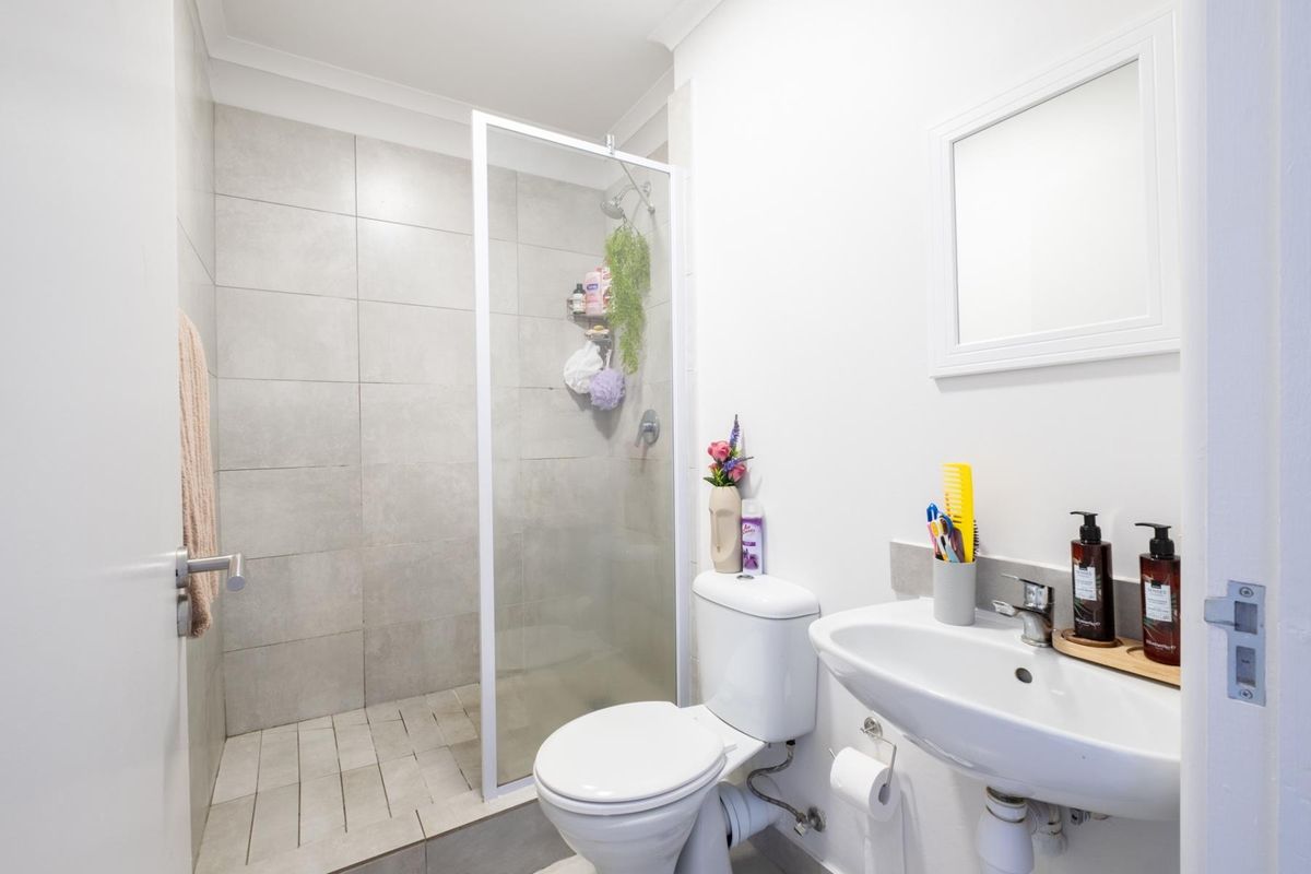 A modern bathroom featuring a walk-in shower with grey tiled walls, a white pedestal sink, and a standard toilet.