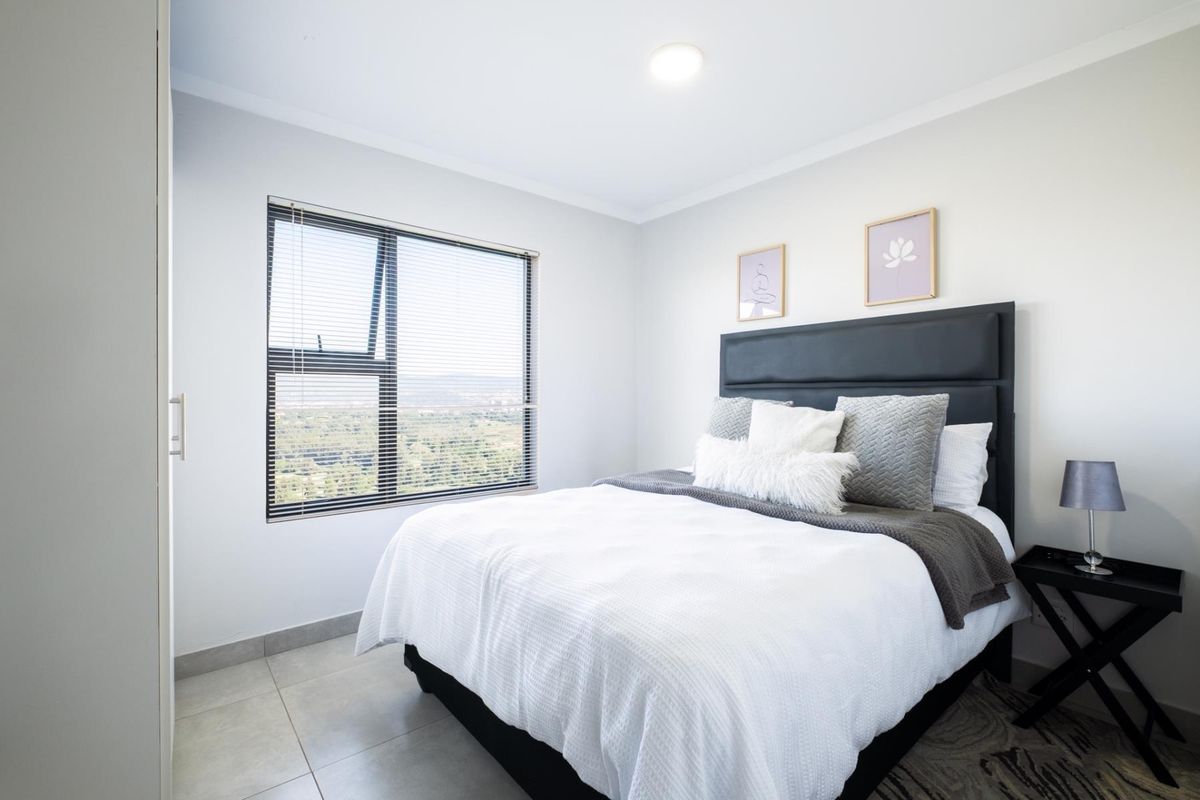A bright and modern bedroom featuring neutral tiled flooring, built-in cupboards, and a large window with views.