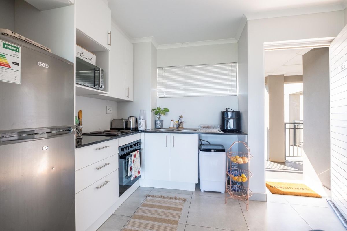 Compact kitchen featuring white cabinetry, dark countertops, built-in oven, and hob, with direct access to an outdoor balcony area.