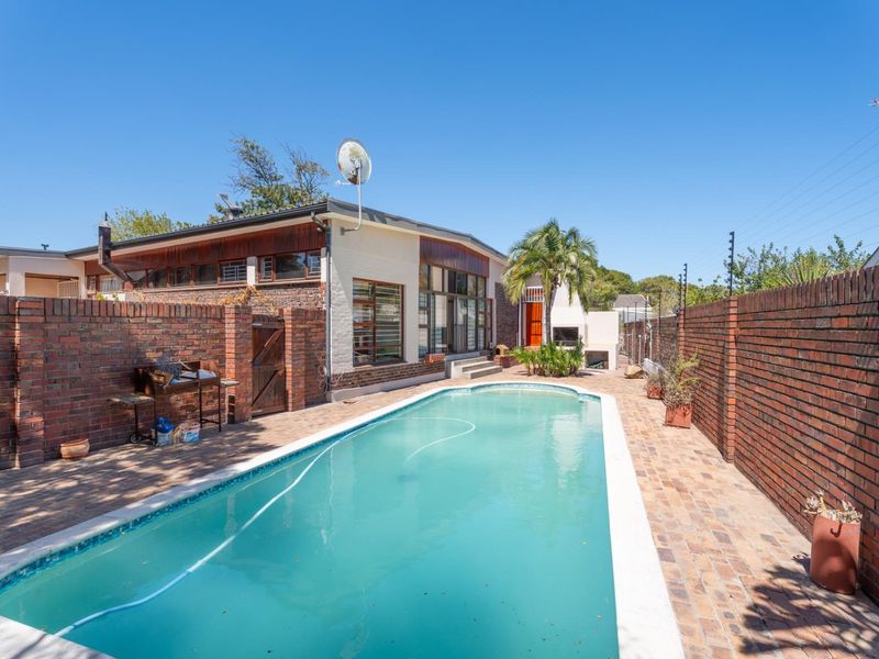Outdoor pool area featuring a paved patio, built-in braai, and secure brick boundary walls with electric fencing.