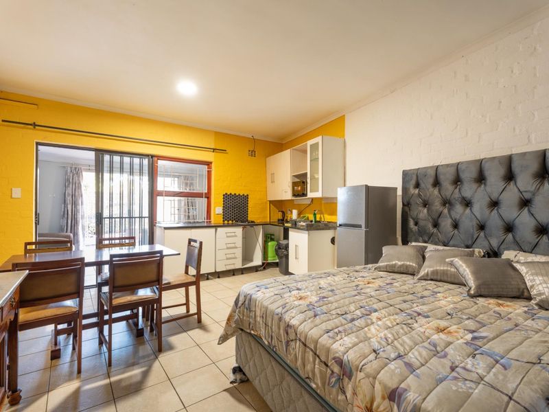 Open-plan studio apartment featuring a compact kitchenette, tiled flooring, and direct access to an outdoor patio area through sliding glass doors.
