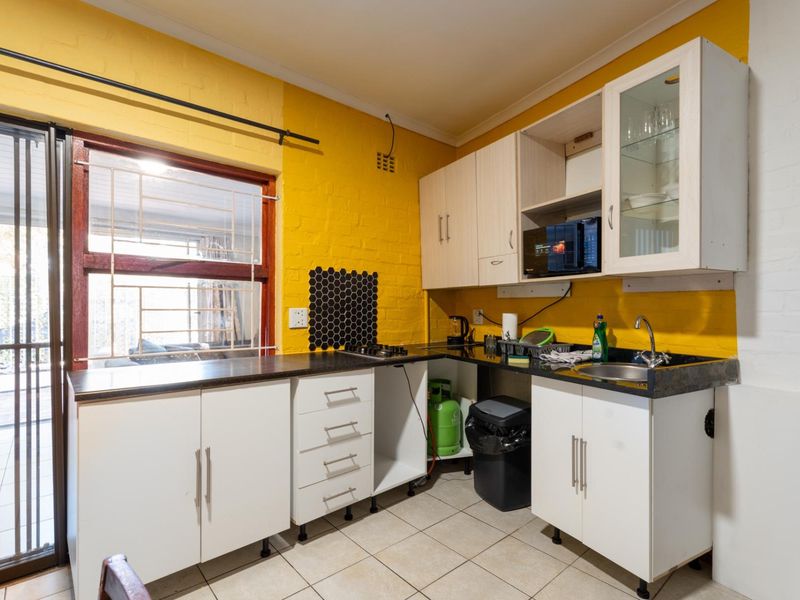 Compact kitchen featuring yellow painted brick walls, white cabinetry, dark countertops, and direct access to an outdoor patio area.