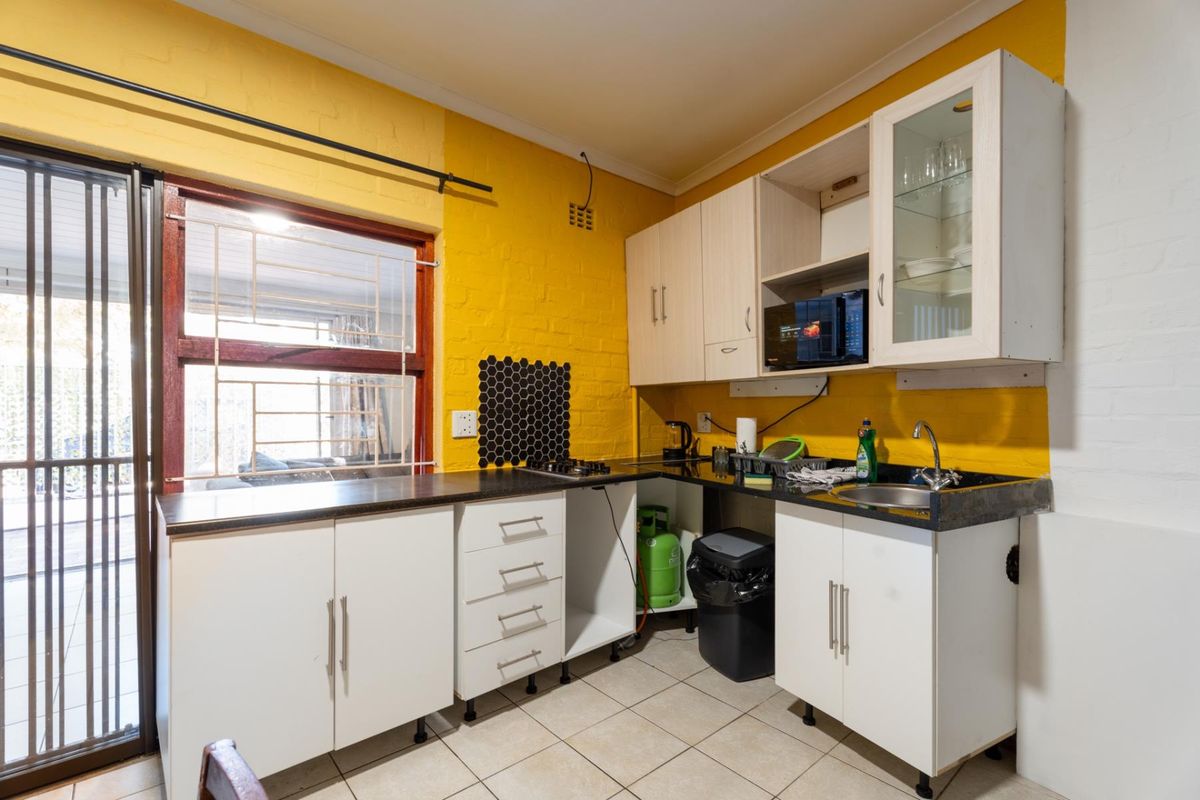 Compact kitchen featuring yellow painted brick walls, white cabinetry, dark countertops, and direct access to an outdoor patio area.