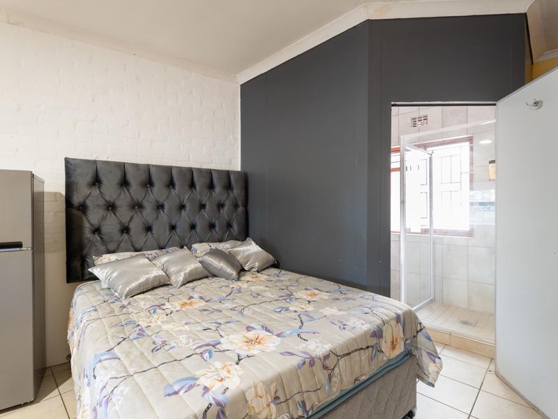Bedroom featuring tiled flooring, a painted brick feature wall, and direct access to an en-suite bathroom with a shower cubicle.