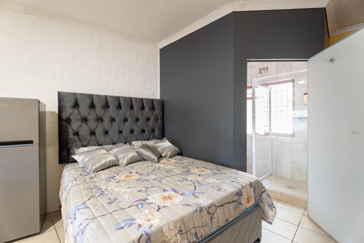 Bedroom featuring tiled flooring, a painted brick feature wall, and direct access to an en-suite bathroom with a shower cubicle.