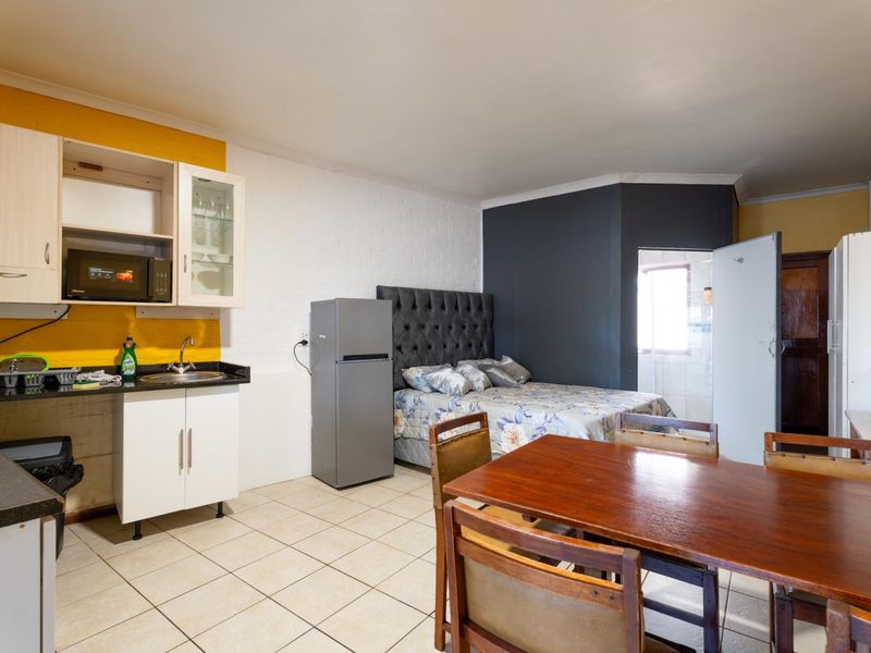 Open-plan studio apartment featuring a compact kitchenette with built-in cabinetry and tiled flooring, seamlessly integrated with the sleeping and dining area.