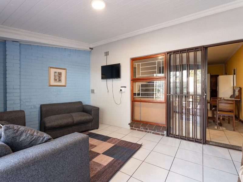 A living area featuring tiled flooring, a painted brick feature wall, and a sliding security gate leading to an adjacent room.