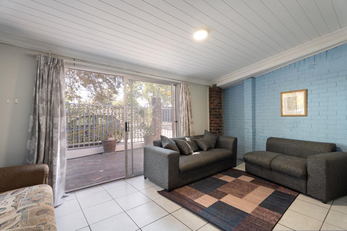A living room featuring tiled floors, a painted brick feature wall, exposed brick detailing, and a sliding glass door leading to an outdoor patio area.
