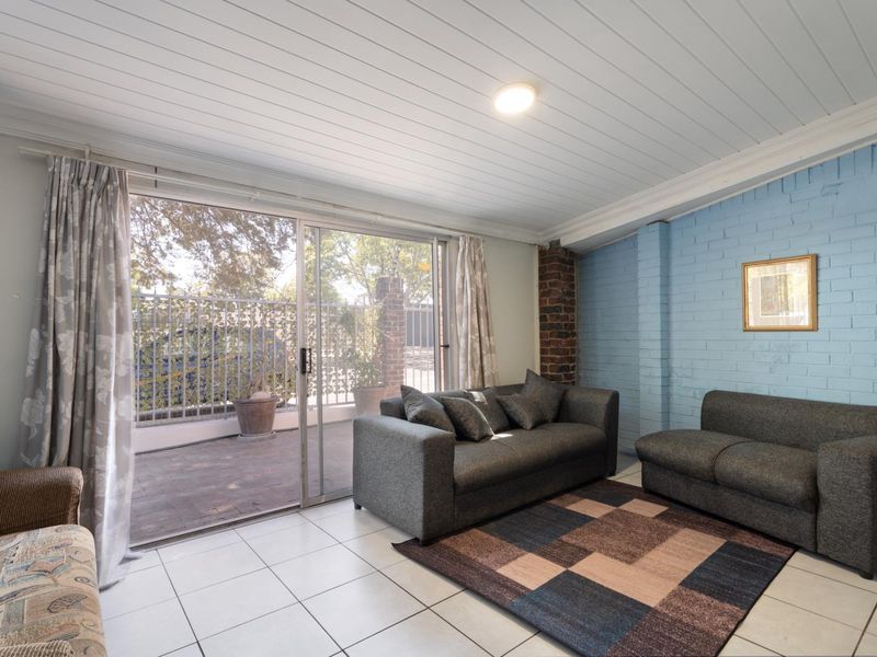 A living room featuring tiled floors, a painted brick feature wall, exposed brick detailing, and a sliding glass door leading to an outdoor patio area.