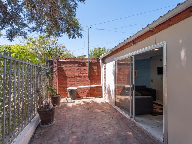 A private outdoor patio area featuring brick paving, enclosed by a metal fence and brick boundary wall, with direct access to the interior living space.