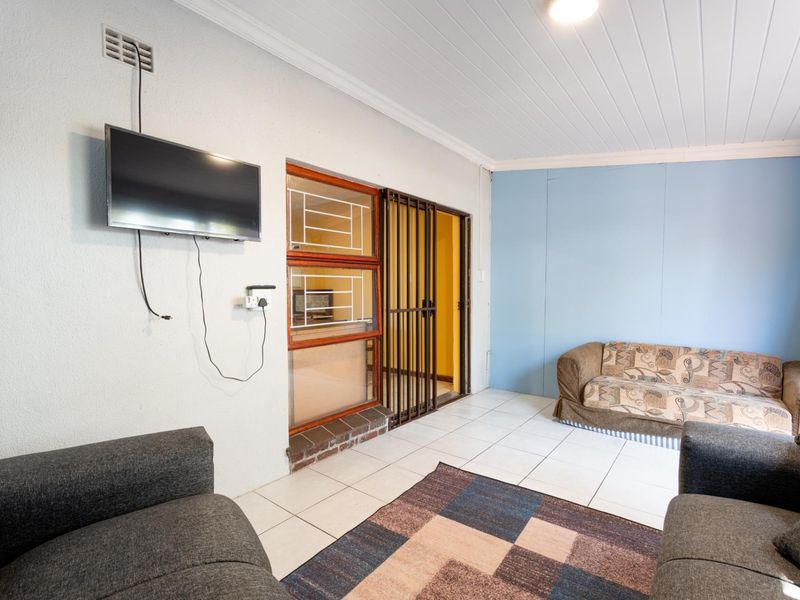 A living area featuring tiled flooring, a security gate, and a brick feature wall, providing a functional space with potential for cosmetic updates.