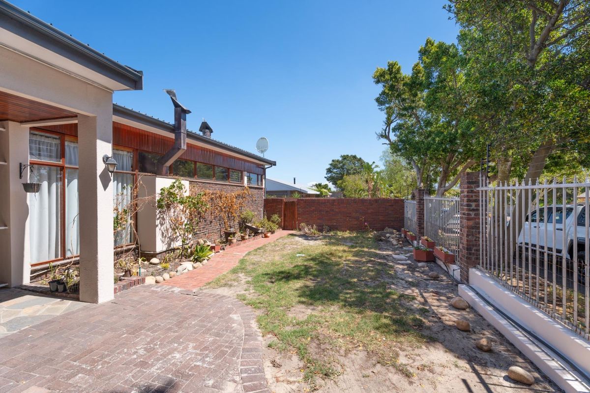 Rear exterior view featuring a paved patio area, brick boundary walls, and metal security fencing with a small garden space.