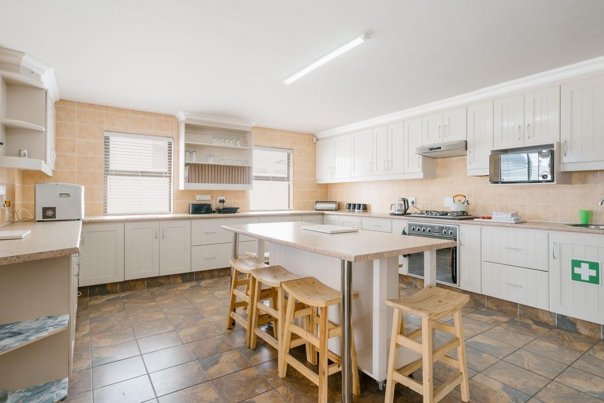 Spacious kitchen featuring white cabinetry, a central island with seating, tiled flooring, and built-in appliances including a stove and extractor fan.