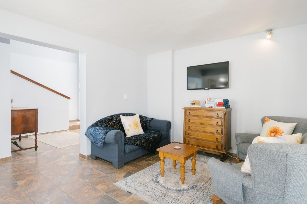 A living room area featuring tiled flooring and a wall-mounted television, with an open transition leading to a staircase.