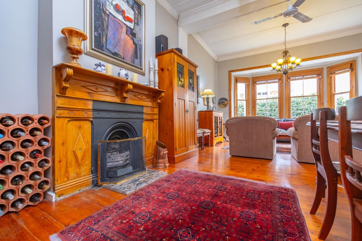 A character-filled living room featuring polished timber flooring, a traditional fireplace with a wooden mantel, and a large bay window providing natural light.