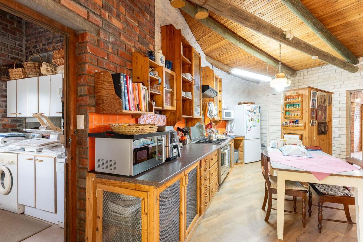 Rustic kitchen featuring exposed brick walls, timber beamed ceilings, wooden cabinetry, and an adjacent laundry area.
