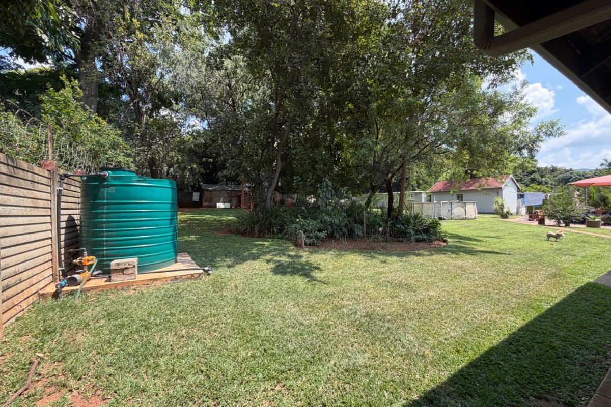 A spacious rear garden featuring a large green water storage tank, mature trees, and a well-maintained lawn area.