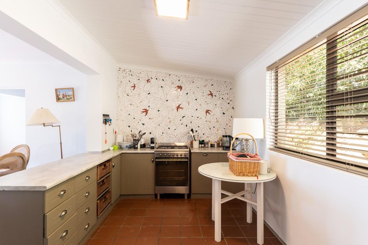 A functional kitchen featuring a built-in oven, tiled flooring, and a decorative mosaic feature wall, with ample counter space and natural light.