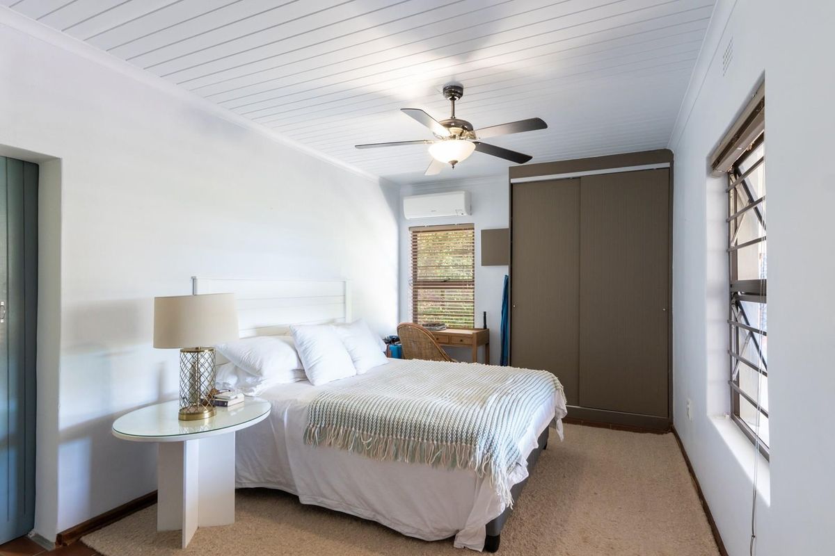 A well-maintained bedroom featuring a built-in wardrobe, ceiling fan, and wall-mounted air conditioning unit, with neutral finishes and ample natural light.