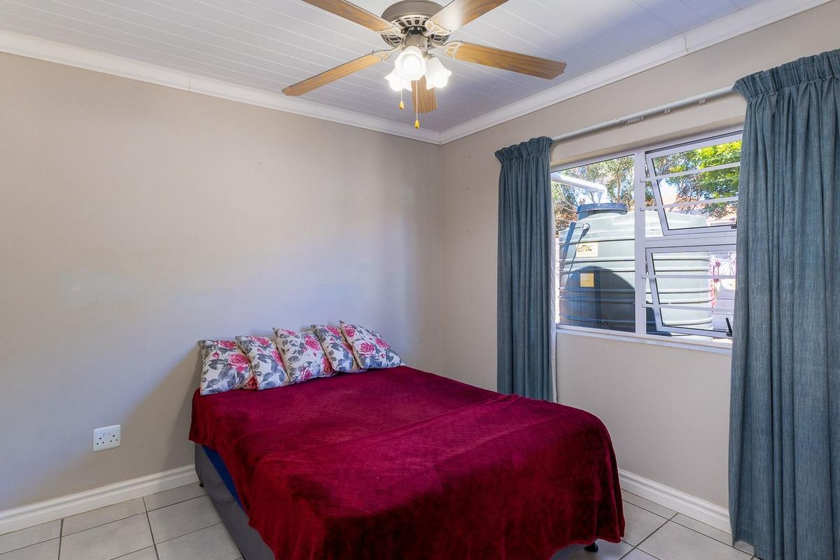 A functional bedroom featuring tiled flooring, a ceiling fan, and a window with views of the exterior water tank.