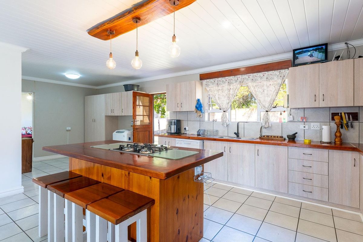 Spacious kitchen featuring a central wooden island with integrated gas hob, ample cabinetry, tiled flooring, and a timber-paneled ceiling with pendant lighting.