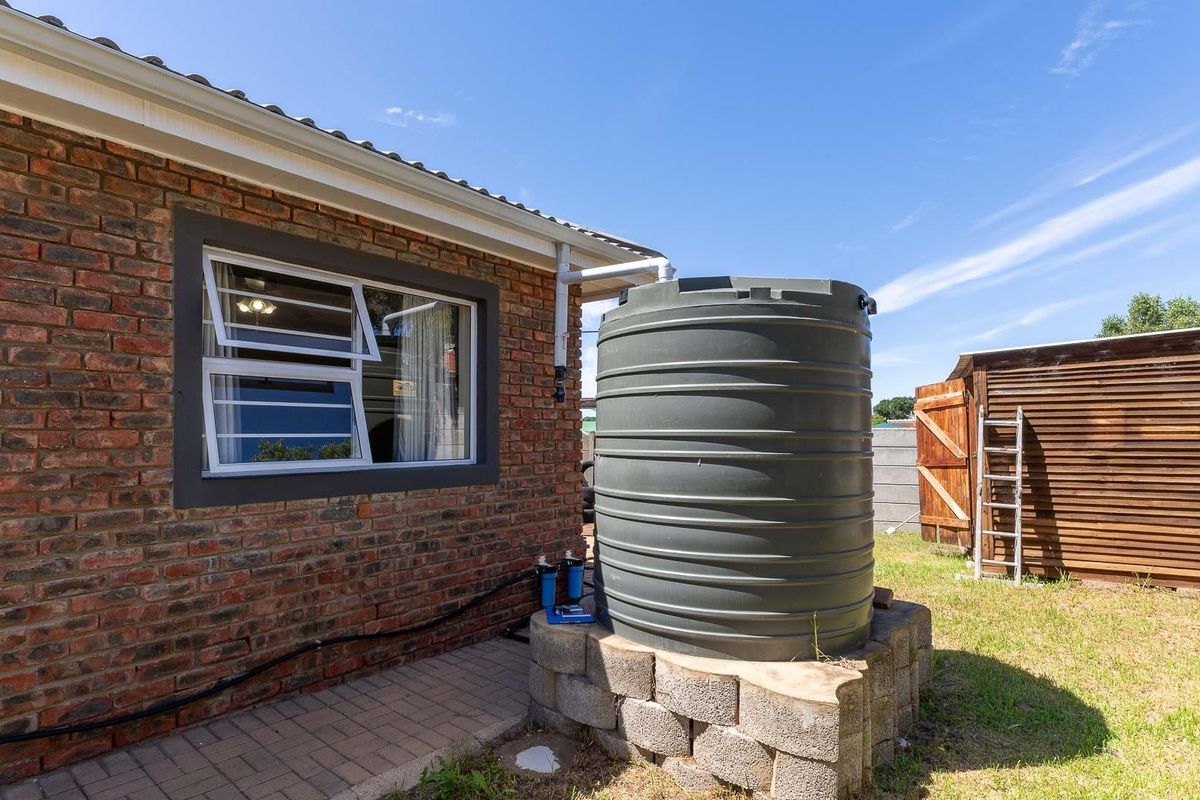 Exterior view of the property featuring a brick facade, a large water storage tank on a concrete block base, and a wooden storage structure.