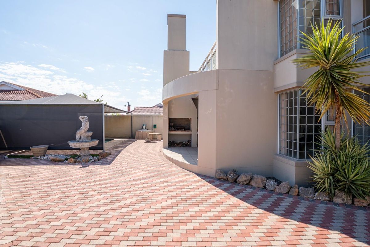Rear exterior view featuring a paved patio area with a built-in braai fireplace and access to the garden space.